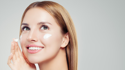 Beautiful female face closeup.Cute girl with healthy skin applying moisturizing cream and looking up. Skincare, beauty and facial treatment concept