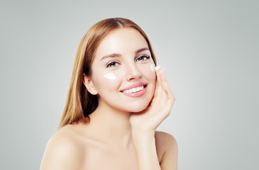 Beauty portrait of cute young woman smiling while applying some facial cream on her cheek