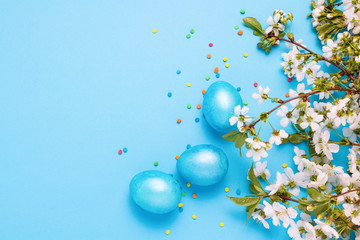 Blooming Cherry Twig, Easter Blue Eggs and Multicolored Powder on the Blue Background