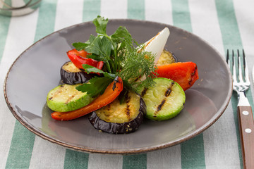 Grilled vegetables zucchini, bell pepper and fresh dill and parsley on the plate on textile background