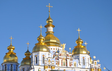 Fototapeta na wymiar Domes and crosses of St. Michael's Golden-Domed Monastery in the sunset light against blue sky.
