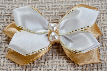 Hairpin for a bow of white and gold color on the background of coarse fabric, closeup shot