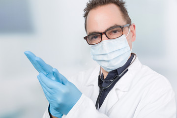 Ein Arzt mit Mundschutz zieht sich hygienische Handschuhe an