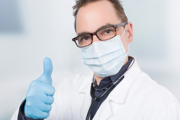 Ein Arzt mit Mundschutz und hygienischen Handschuhen zeigt Daumen hoch