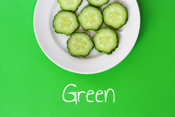 Top view of a plate with sliced cucumber slices on a green background.