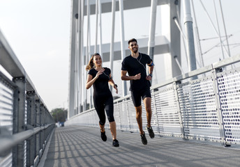 Young couple in black sports outfit doing morning workout outdoors. Young man and woman running on...