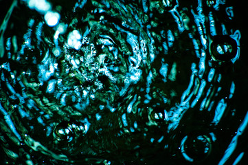 Macro shot of abstract, blurred, blue water background. Water flow and drops falling from the tap water in a large bowl. Beautiful gentle wave motion in the pool. Bubbles, round circles, wavy lines