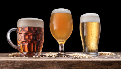 Glasses of beer on old wooden table. Black background.