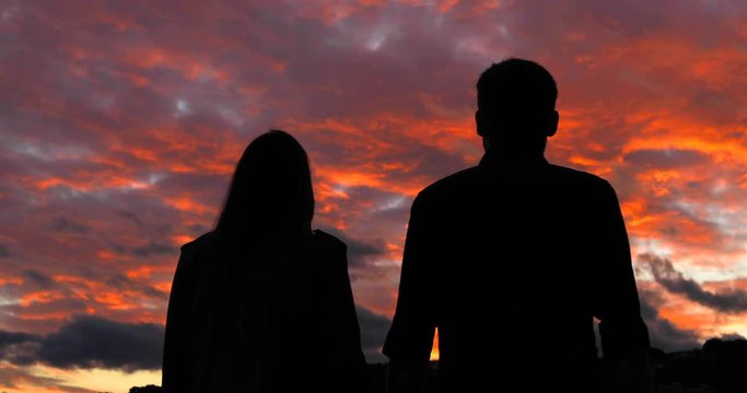 Back view silhouette of an excited couple walking and raising arms at sunset