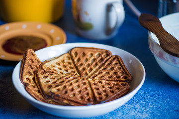 Macro shot of just cooked, delicious, tasty and hot yogurt pancakes with strawberry sauce on yellow and white plates in kitchen, next to stove. Dinner is ready. Sweet golden brown waffles with jam
