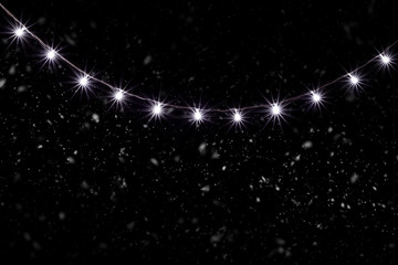 Fototapeta premium Christmas Lights, Garland in Snowfall with Small Led Lamps Shining on Black Background.