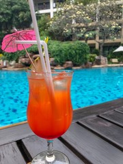 Glass of tequila sun rise cocktail on wooden table beside swimming pool with pineapple sliced put on 