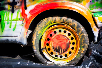 Shot of colorfully painted car tire on an old, crashed car wreck. Kids are having fun, making...