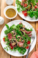 Fresh light vegetable salad with arugula lettuce, mushrooms, cherry tomato and cured ham