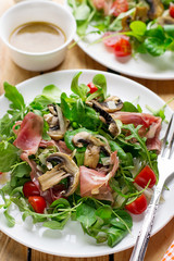 Fresh light vegetable salad with arugula lettuce, mushrooms, cherry tomato and cured ham