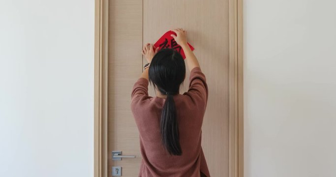 Woman stick red chinese calligraphy on the door for lunar new year, word means luck