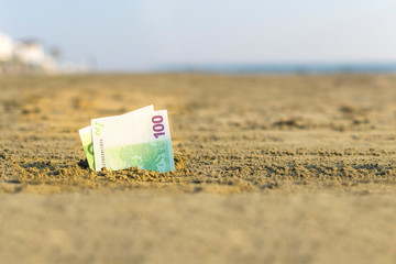 Banknote of value of one hundred euro in the the sand on the beach. Concept of cheap travel and vacation. Promotion and discount