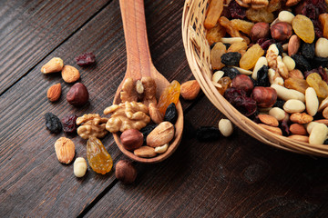 Dried fruits and nuts on a wooden background in a wicker basket with a wooden spoon