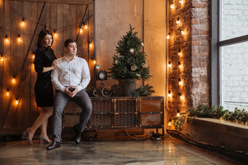 Happy couple of lovers  sit on the windowsill. Christmas atmosphere at home. Young family together. Garland lights in the foreground bokeh