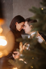 Happy couple of lovers  sit on the windowsill. Christmas atmosphere at home. Young family together. Garland lights in the foreground bokeh