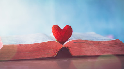 red heart in bible on wooden table, love of christian concept.