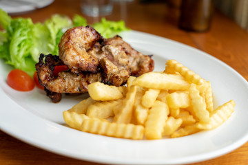 Grilled Pork and French Fries, arranged on a beautiful white food dish with salad vegetables, looking to eat Western main dishes. Popular with many