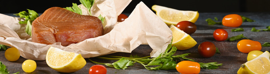 A piece of smoked tuna on brown paper, near vegetables.