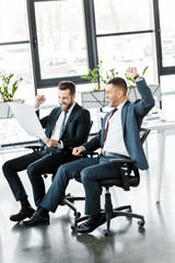 happy businessmen looking at paper and celebrating victory in modern office