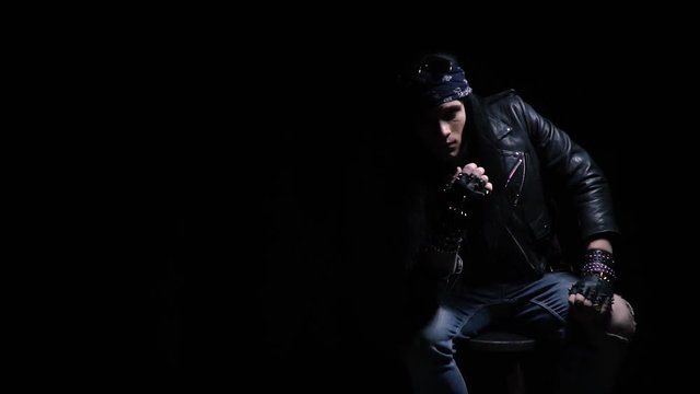 Posing rocker guy with long black hair, wearing leather jacket and spiked gloves, slow motion