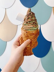 Hand with Fish shaped ice-cream with chocolate and mint creamy ice-cream on a colorful fish flakes background