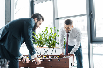smiling businessmen playing table football in modern office