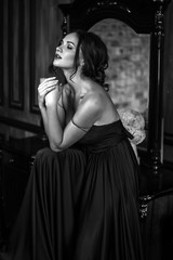 Portrait of young woman in elegant silk black dress posing in a dark interior, fashion beauty photo