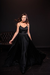 Portrait of young woman in elegant silk black dress posing in a dark interior, fashion beauty photo