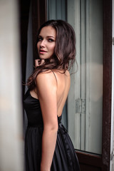 Fototapeta na wymiar Portrait of young woman in elegant silk black dress posing in a dark interior, fashion beauty photo
