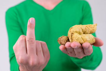 Hands of young man showing middle finger while holding artificial poo