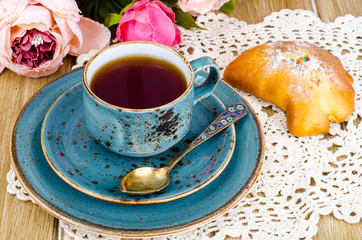 Fresh bun and cup of tea on wooden table for breakfast