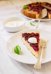 Homemade cherry pie served with cream on a light background with cherry leaves and flowers.