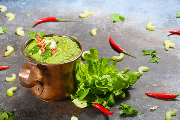 Green vegetarian soup in copper cup on dark background. Horizontal.