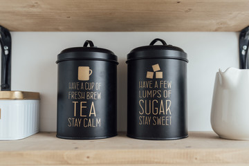 black jars for sugar and tea are on a wooden shelf