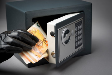 Thief hand with money banknotes during safe code breaking.  Hacking safe