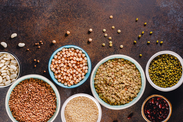 Top view on bowls with various raw grains and seeds on a textured dark background.