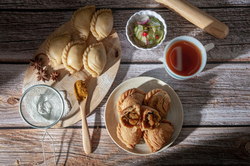 Traditional curry puffs stuffed chicken with raw curry puffs on wooden table as background