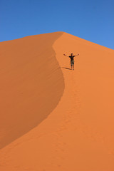 A male traveler in sportswear is standing on the orange sand of a dune in Sosusfle National Park, Namibia.