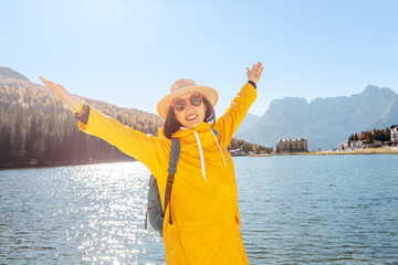 Young happy asian woman with yellow jacket travel at the famous tourist destination in Dolomites mountains - Misurina lake during autumn.