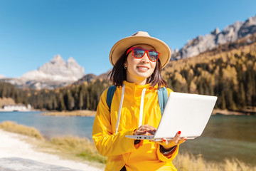 Happy Asian woman working on laptop on mountain lake background in autumn. The concept of remote...
