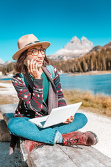 Happy Asian woman working on laptop on mountain lake background in autumn. The concept of remote...