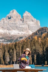 Happy Asian woman working on laptop on mountain lake background in autumn. The concept of remote work and freelancer
