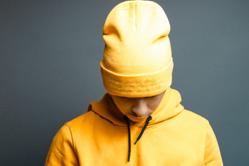 junger Rapper mit gelbem Kapuzenpullover und Beanie Cap senkt den Kopf