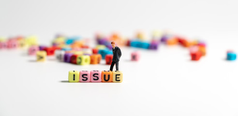 Select focus of colorful of ISSUE alphabet and  looking and miniature figure businessman in dark blue suit standing behind ISSUE alphabet and thinking of ways to solve the problem.