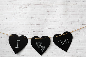 Three hearts hang on a rope, on a brick light wall. The composition of the inscription for Valentine's Day or for the wedding - I love you.